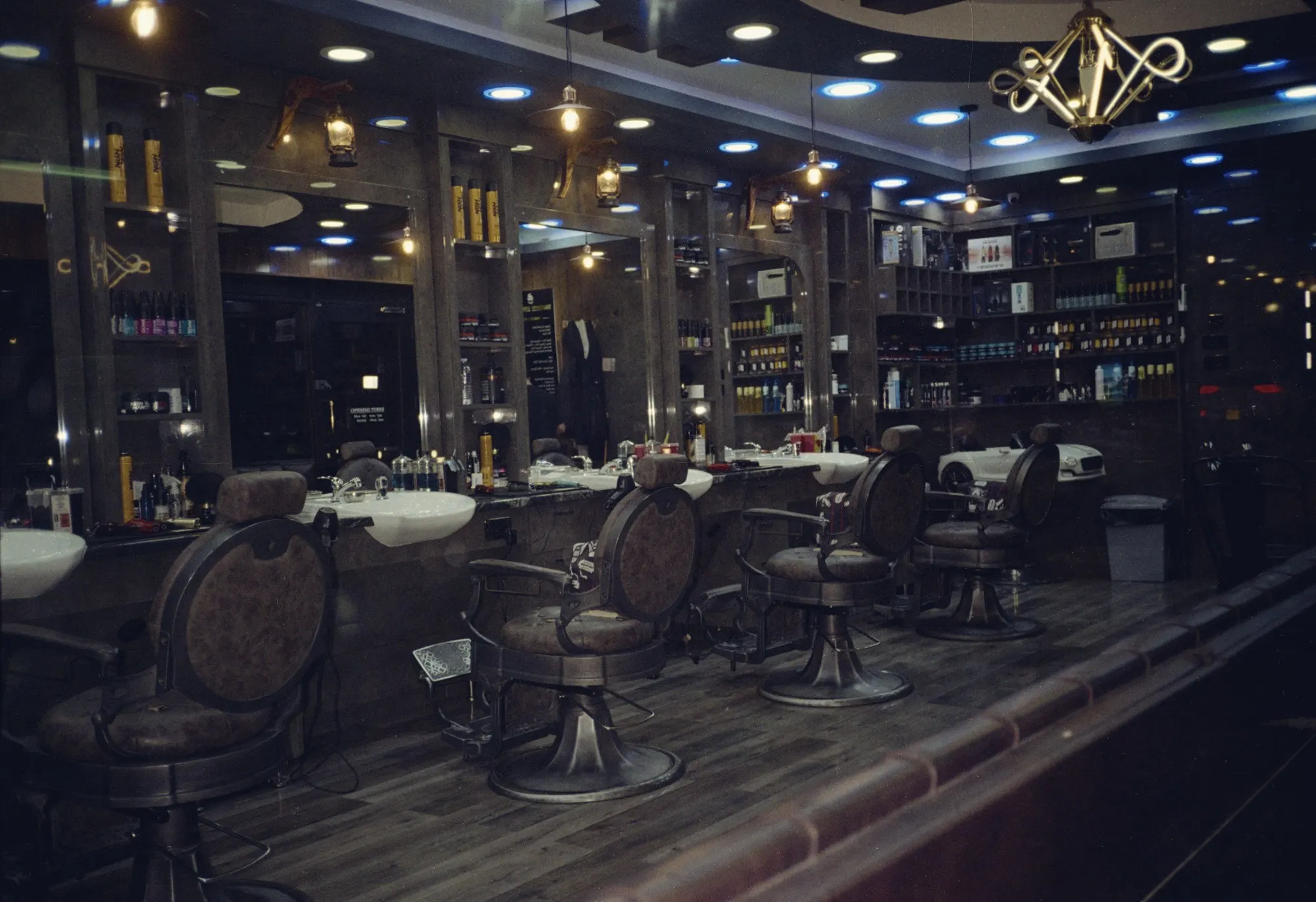 Empty barber shop at night with leather barber chairs, mirrors and product shelves.