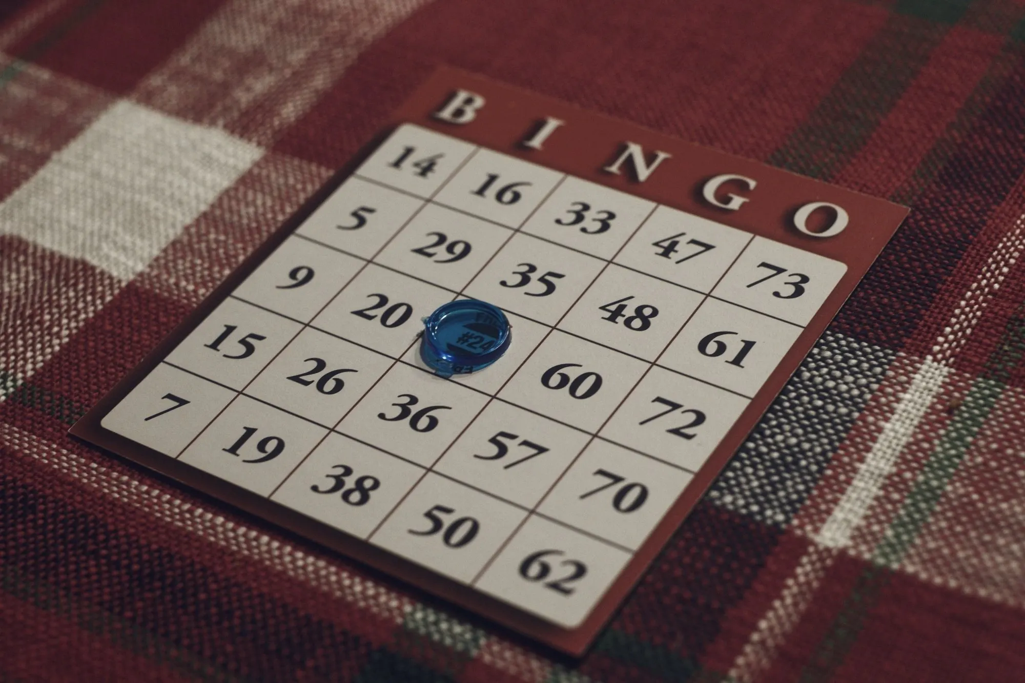 A bingo card on a red plaid cloth with a blue marker on one number.