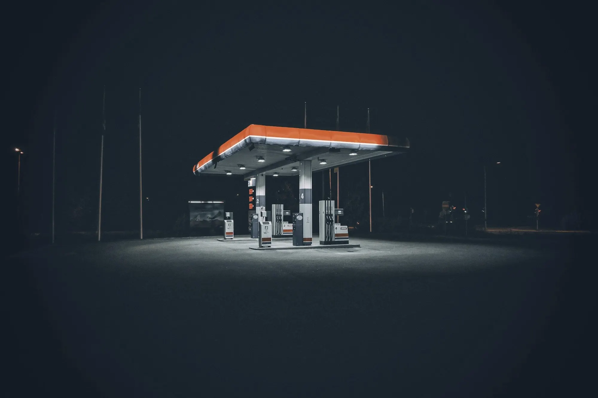A lone fuel station canopy lit up against a dark empty lot at night.