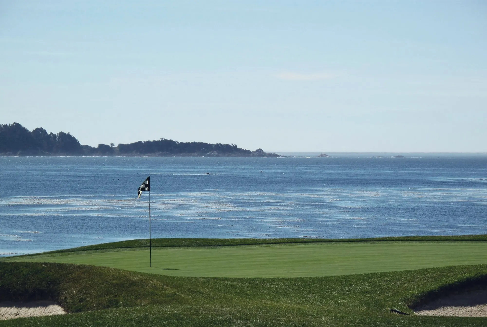 A golf green with a flag above the Pacific Ocean on the California coast.