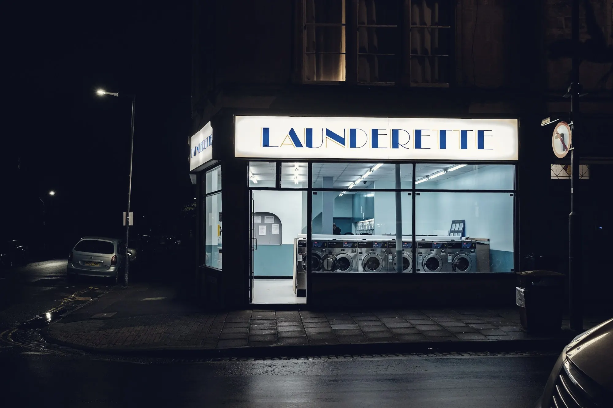 A laundromat storefront glowing at night with rows of washing machines inside.