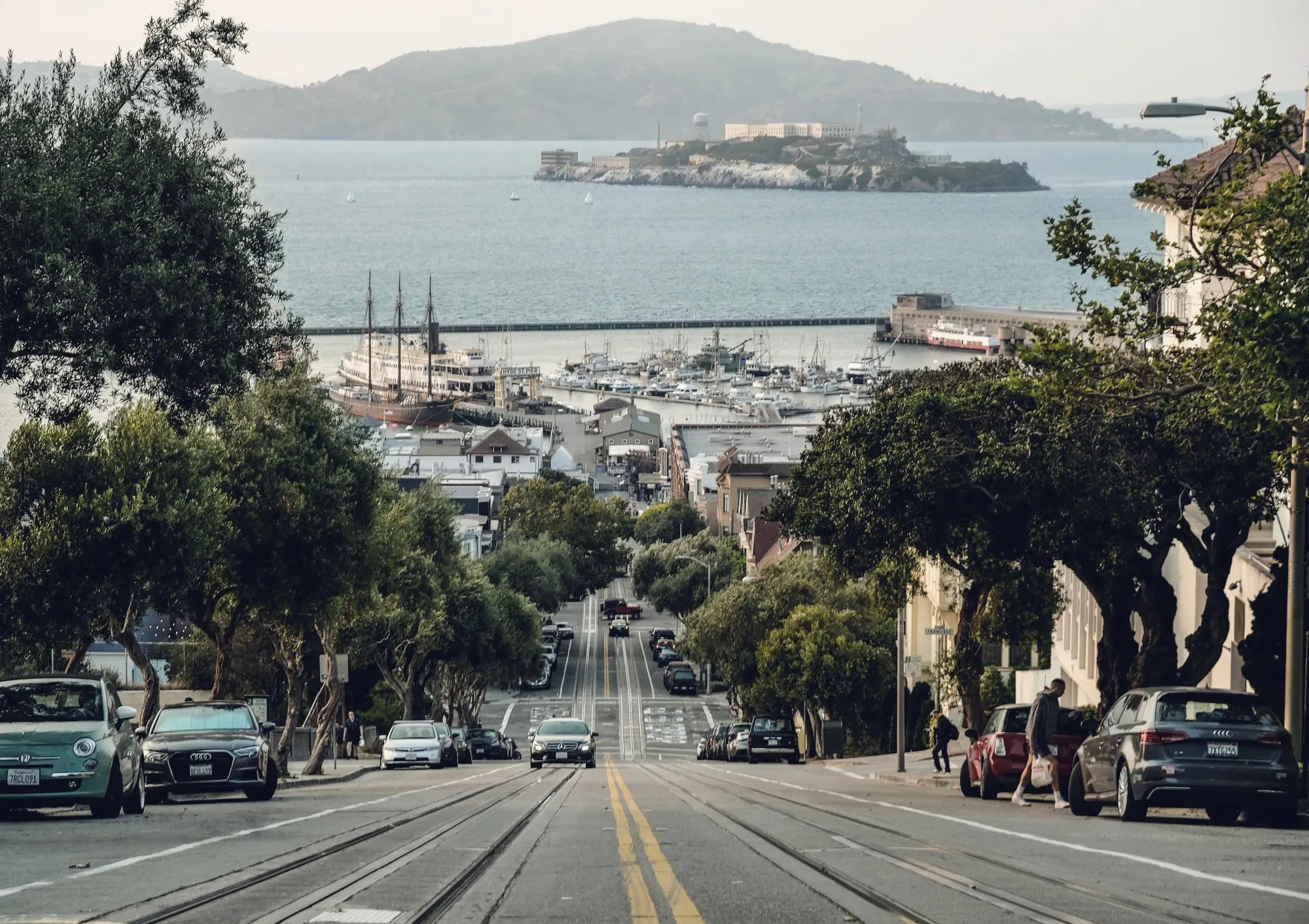 A steep San Francisco street descending toward the bay with Alcatraz Island beyond.