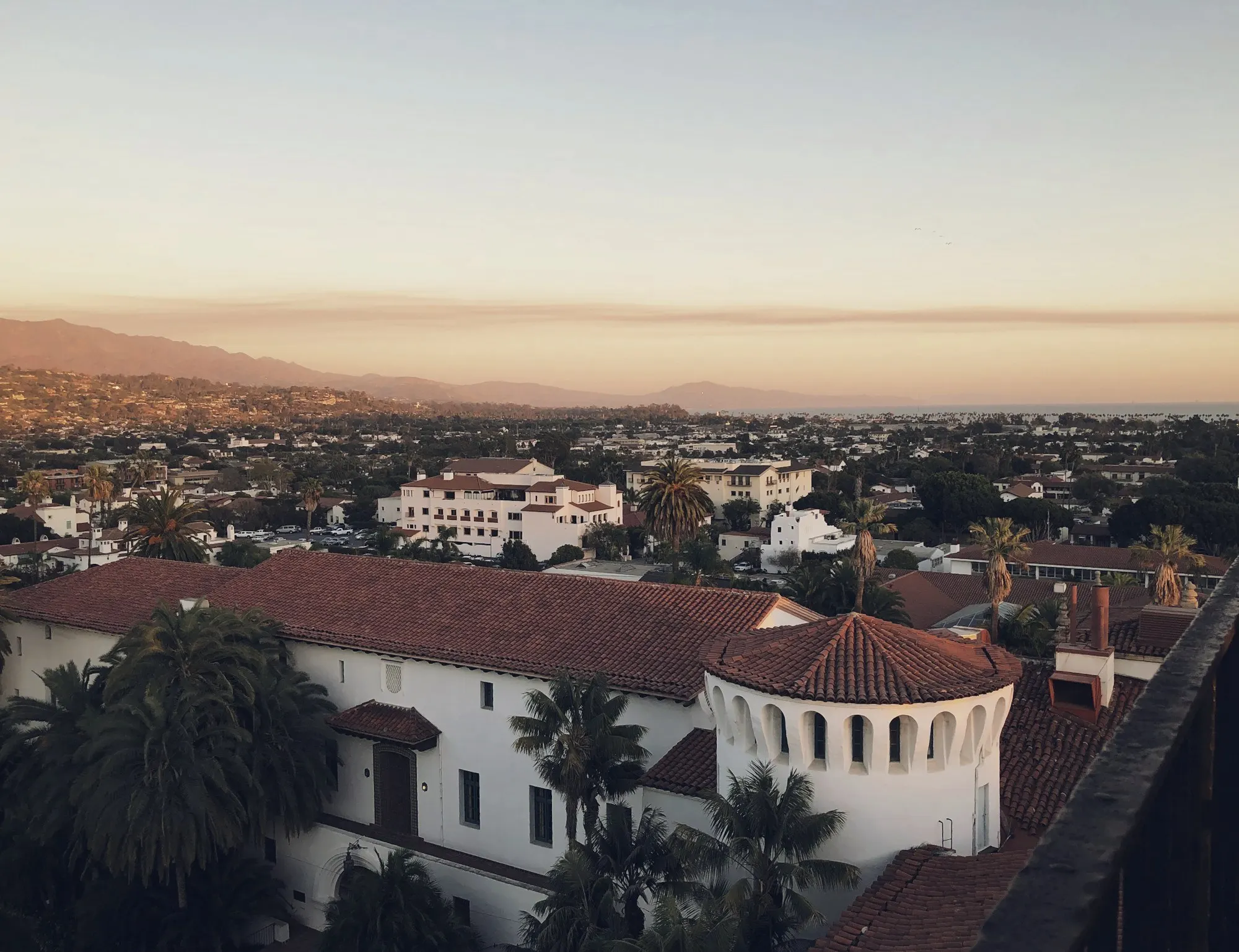 Red tile rooftops of Santa Barbara at sunset with mountains on the horizon.