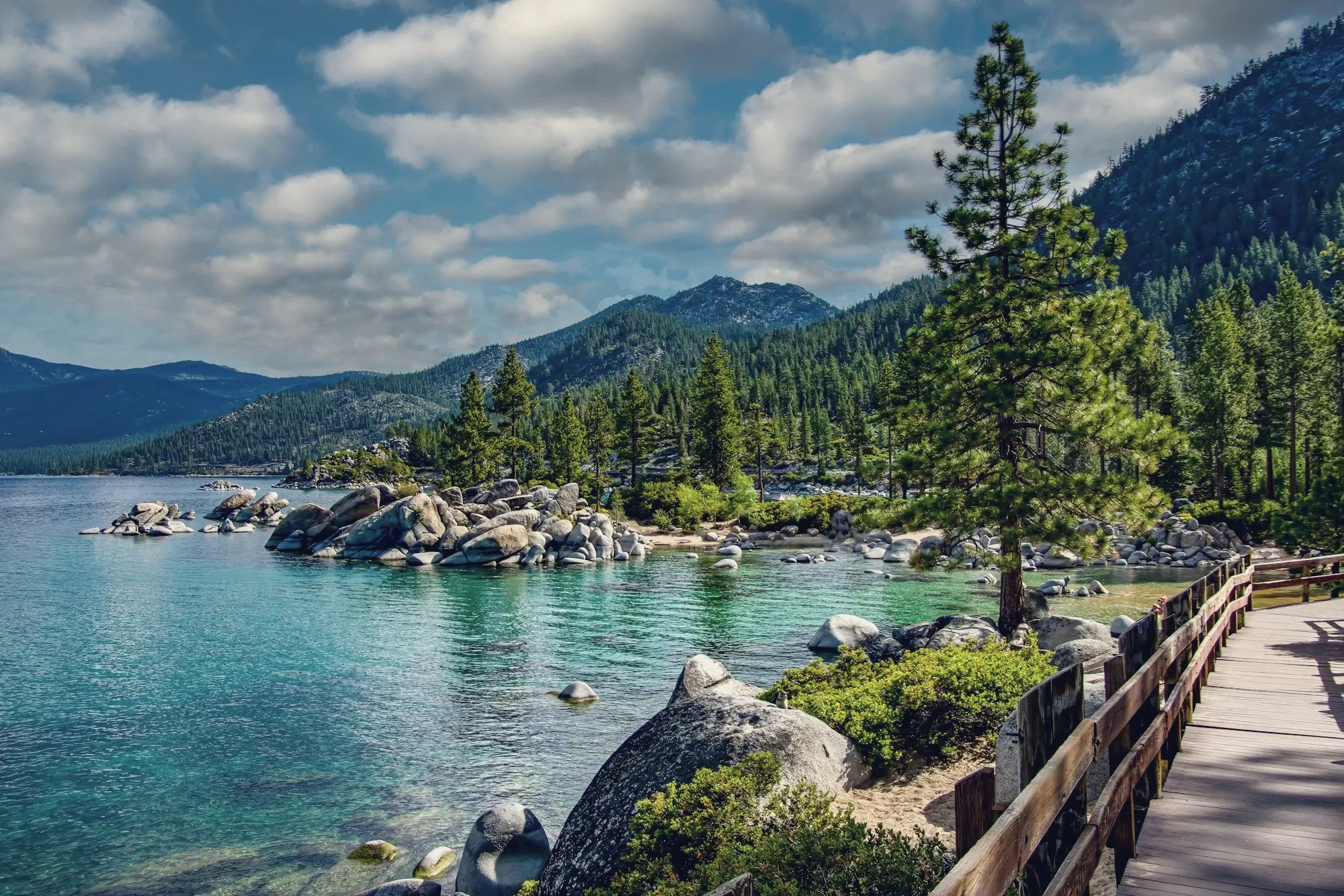 Clear turquoise water and granite boulders along the Lake Tahoe shore with pine trees.