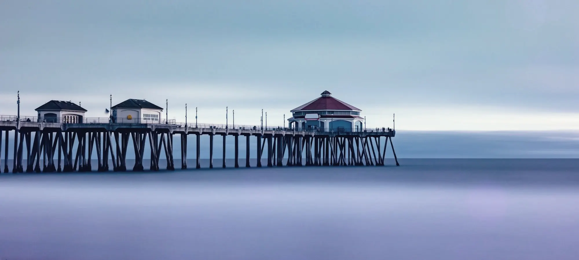 Huntington Beach Pier stretching over calm, misty ocean water under a pale sky.