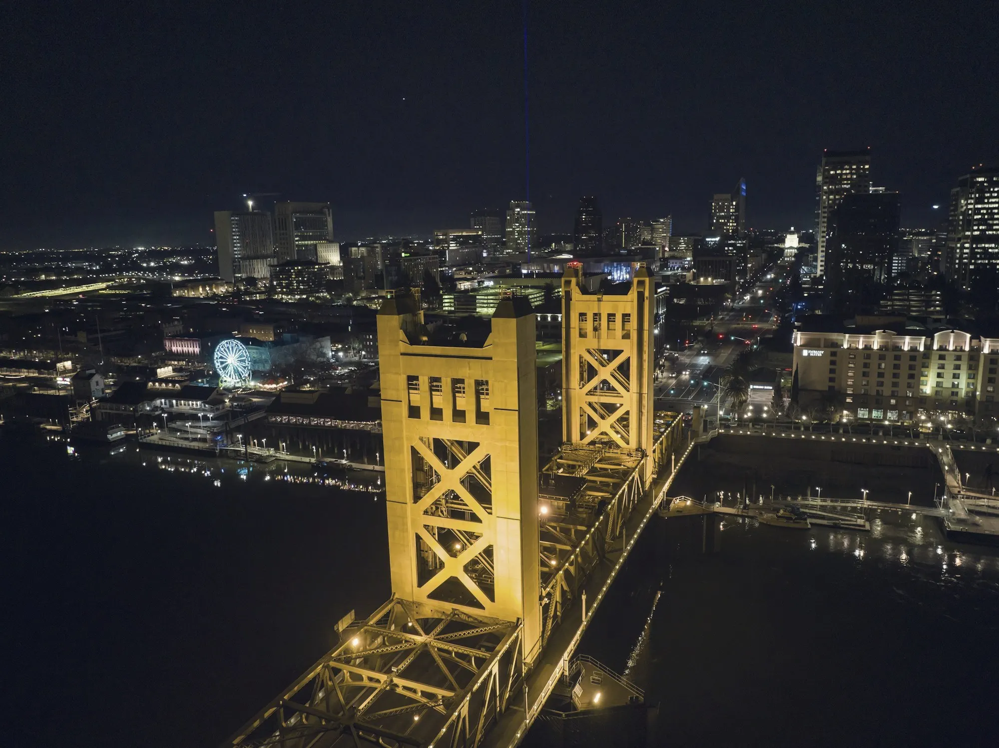 The illuminated Tower Bridge and downtown Sacramento skyline reflected on the river at night.