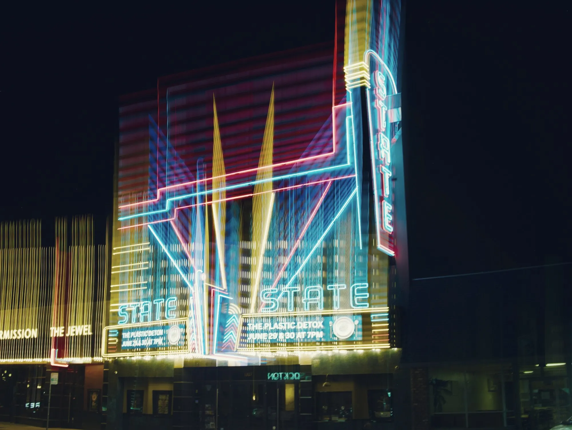 A glowing neon art deco theater facade on a downtown street at night.