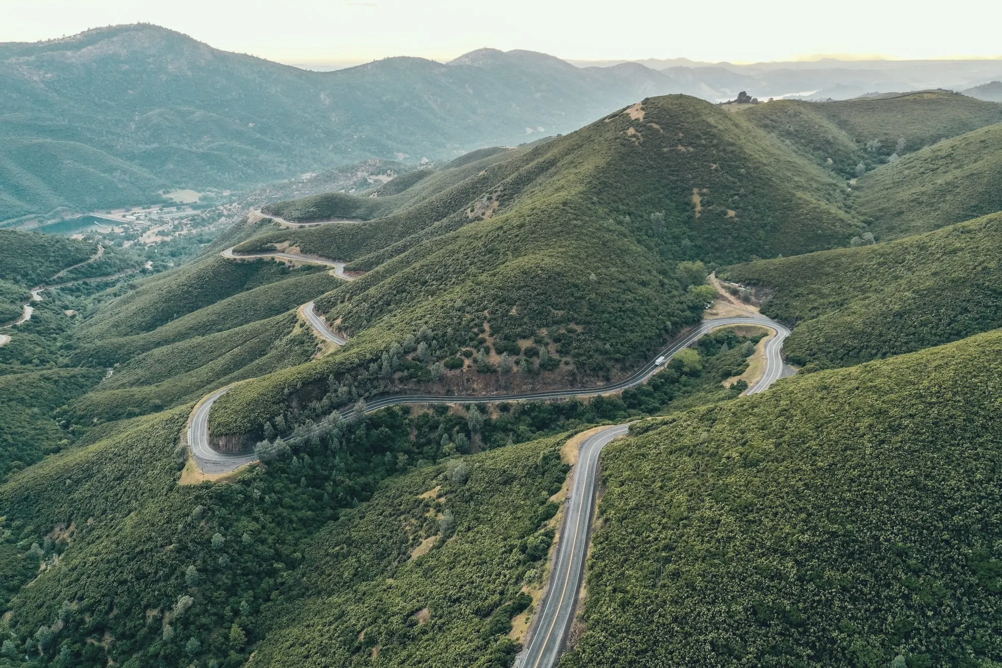 Aerial view of a winding road switchbacking across green mountain ridges.