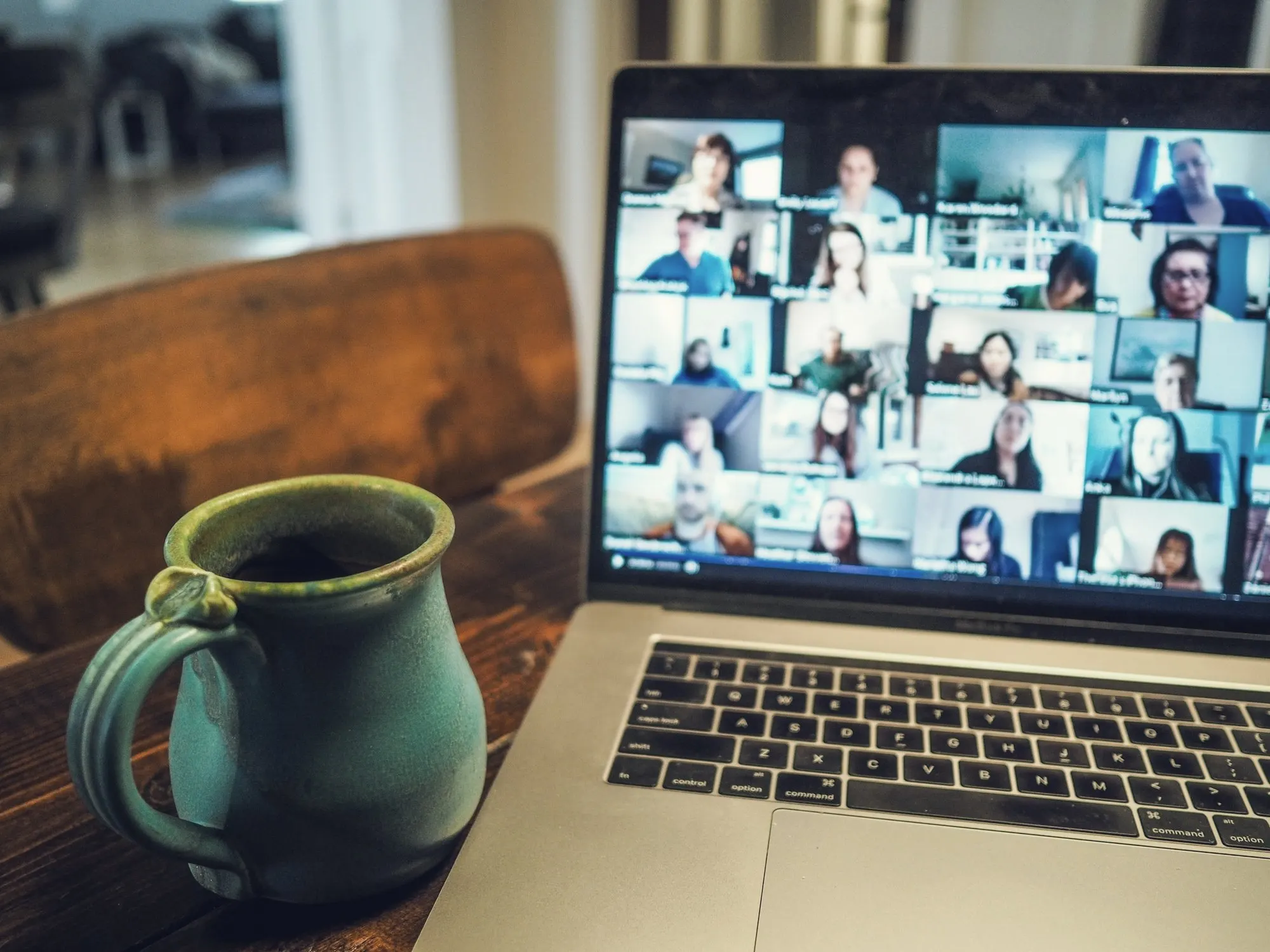 A laptop showing a video call grid beside a green mug on a wooden table.