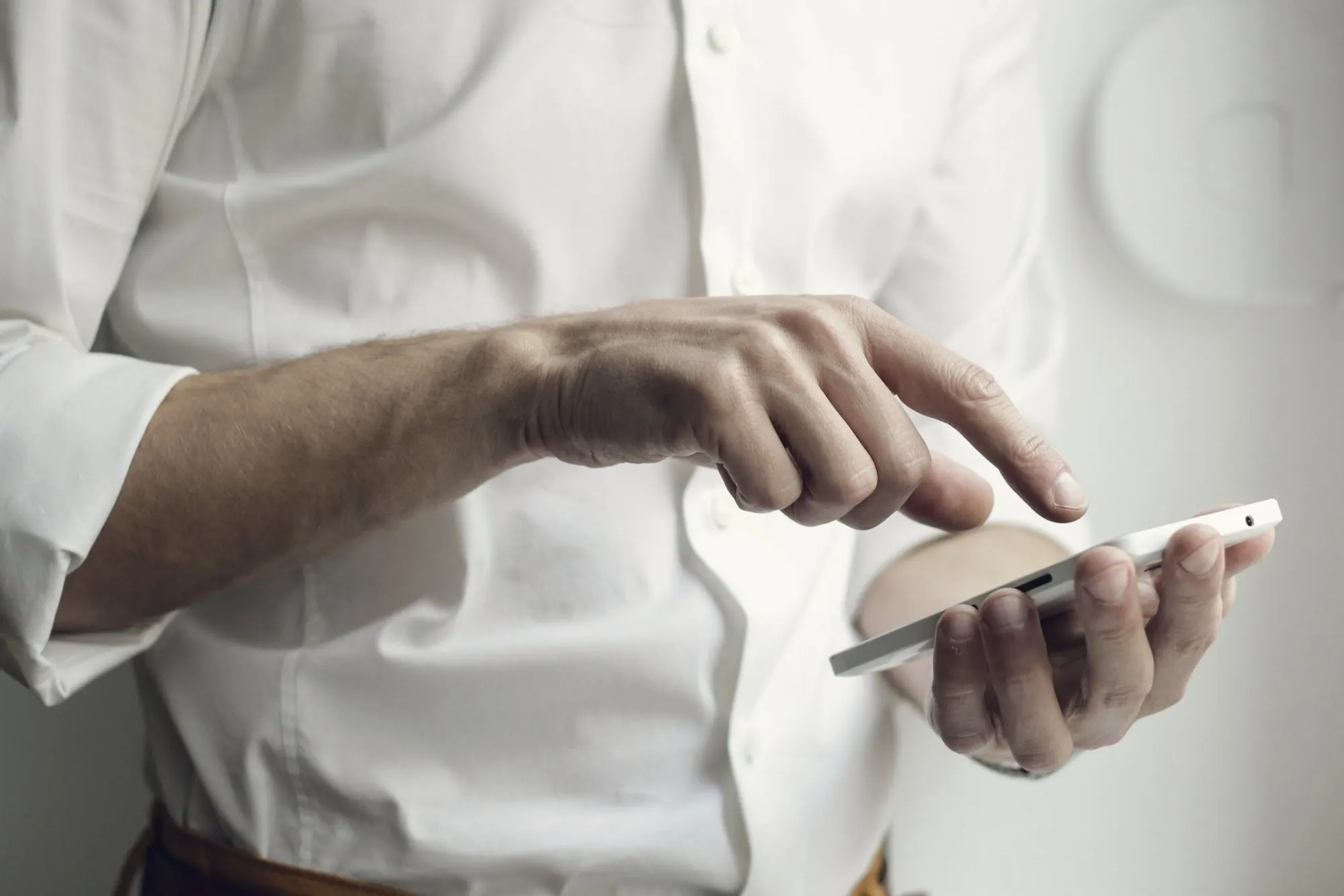 Person in a white shirt tapping a smartphone screen held in one hand.