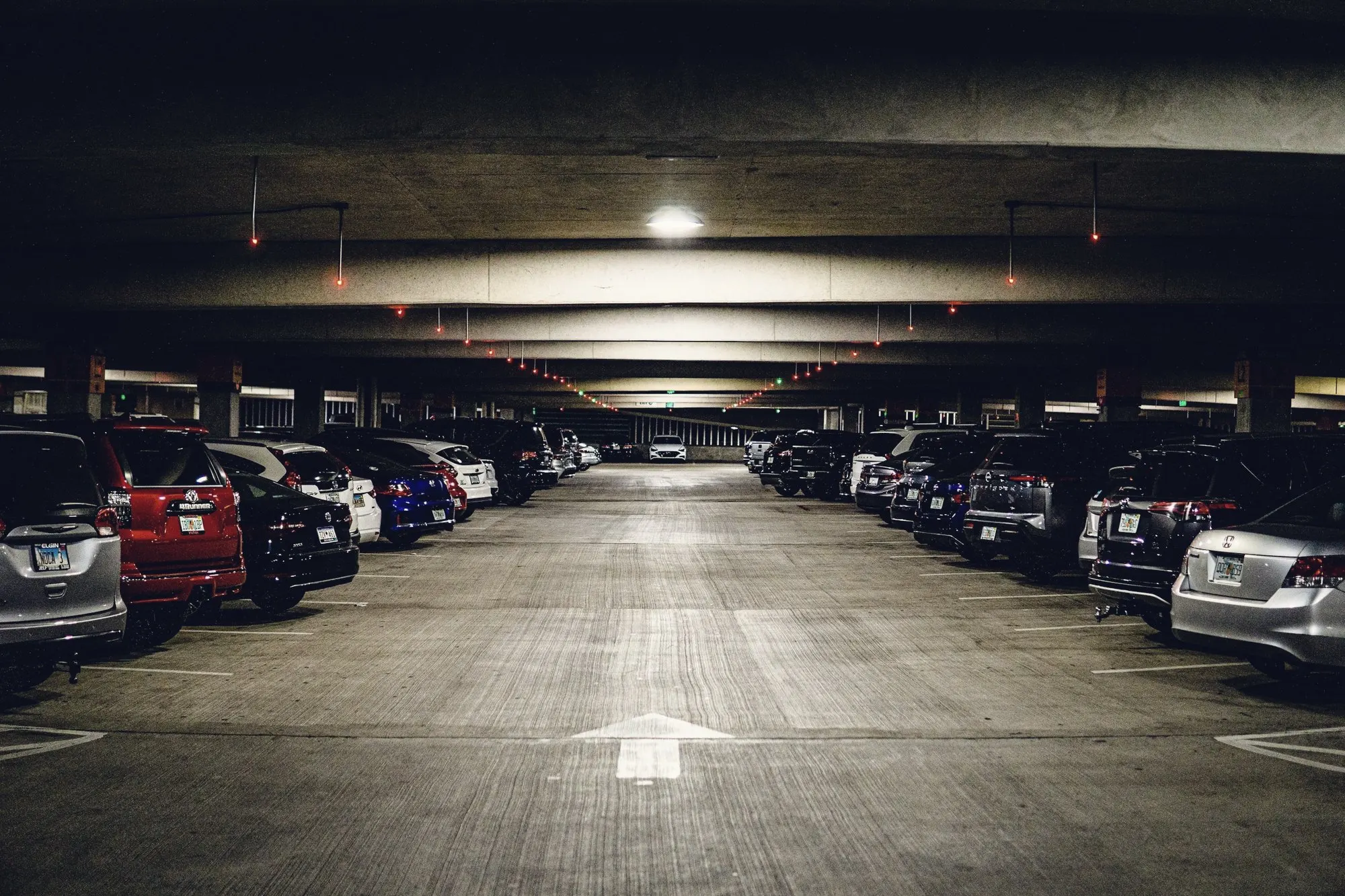 Rows of parked cars inside a lit concrete parking garage with a direction arrow.