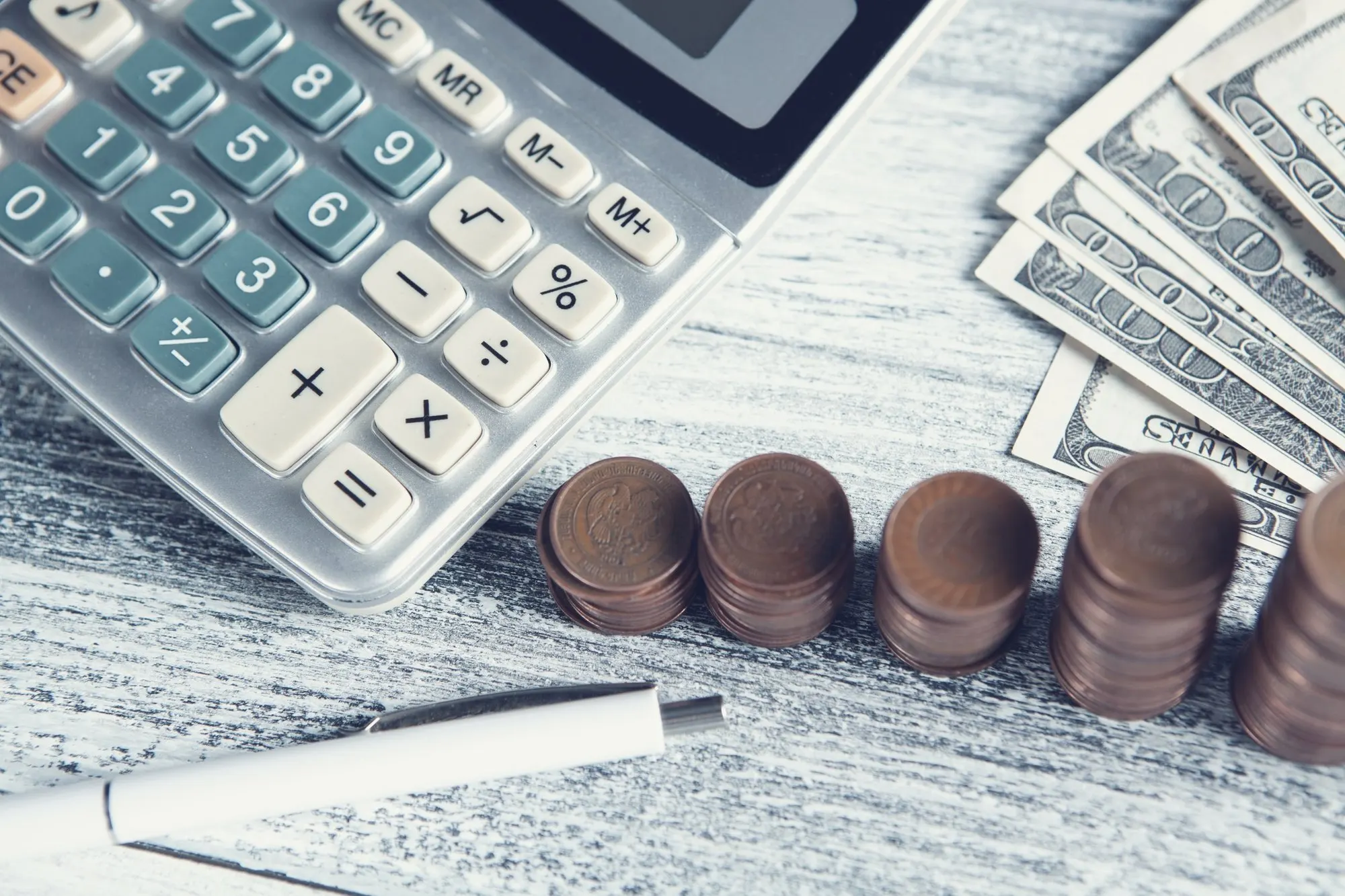 A calculator beside stacked coins and paper money on a desk.