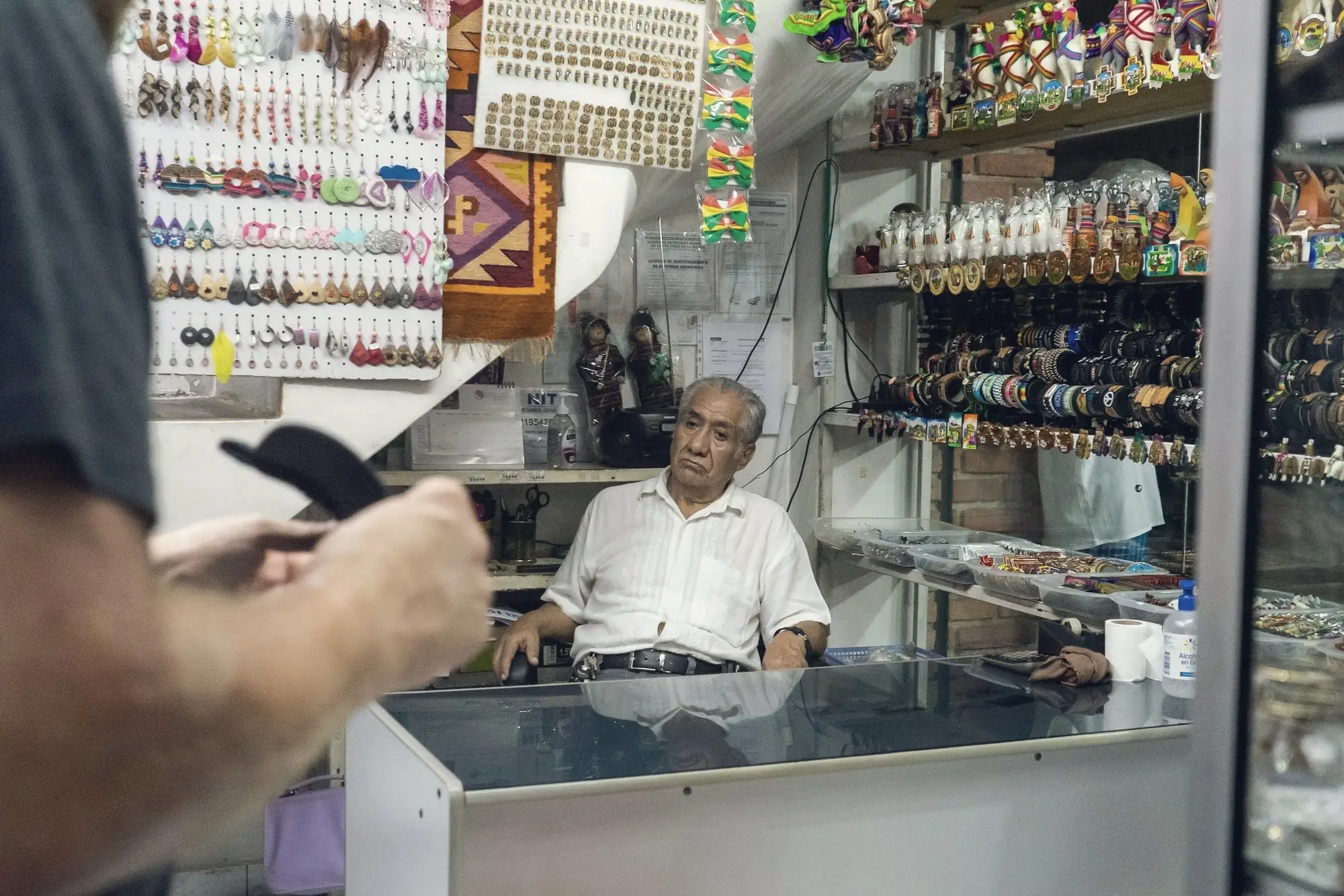 A shopkeeper behind a glass counter in a small crowded store.
