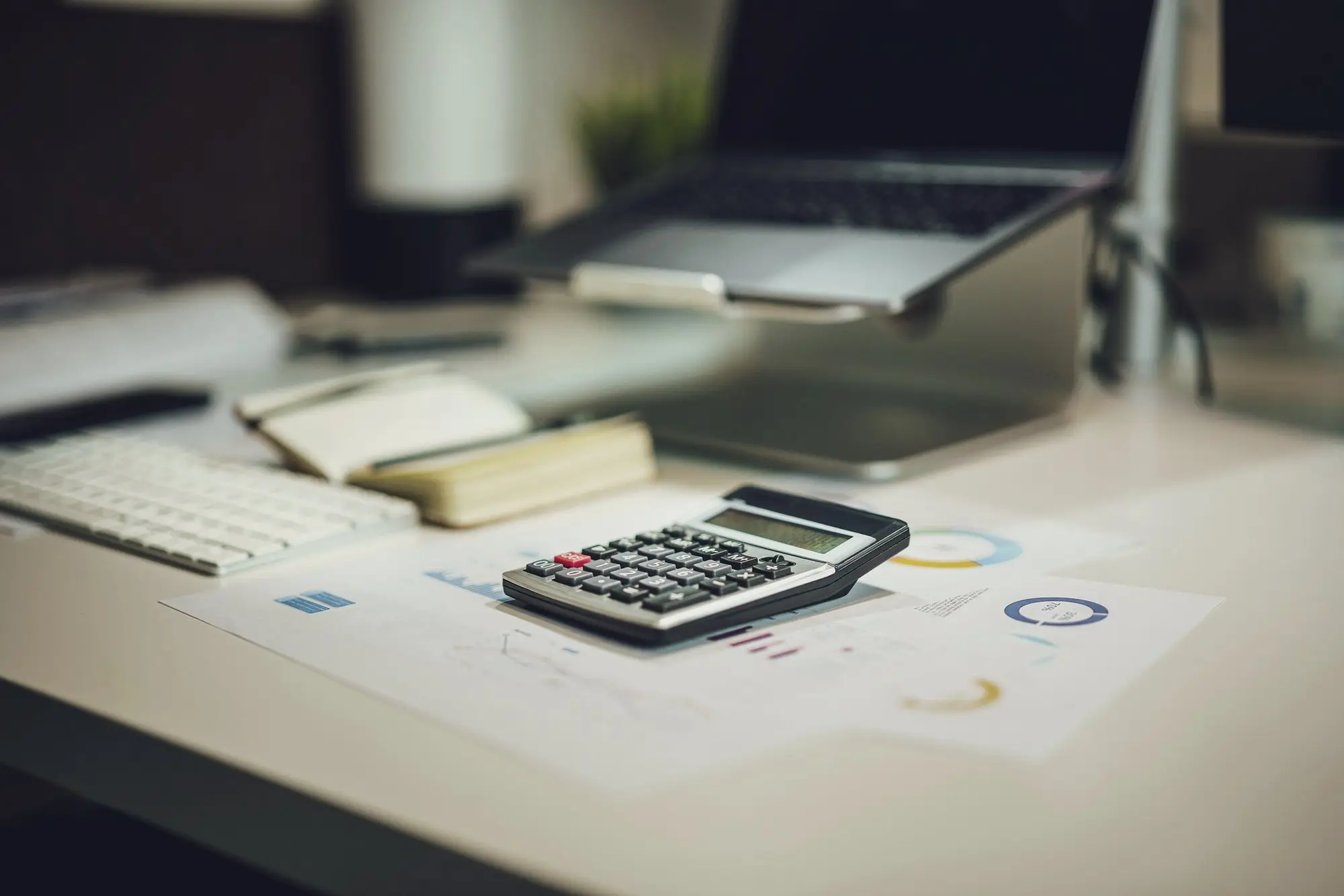 A desk with a laptop, a calculator, notes and printed charts for planning a business.