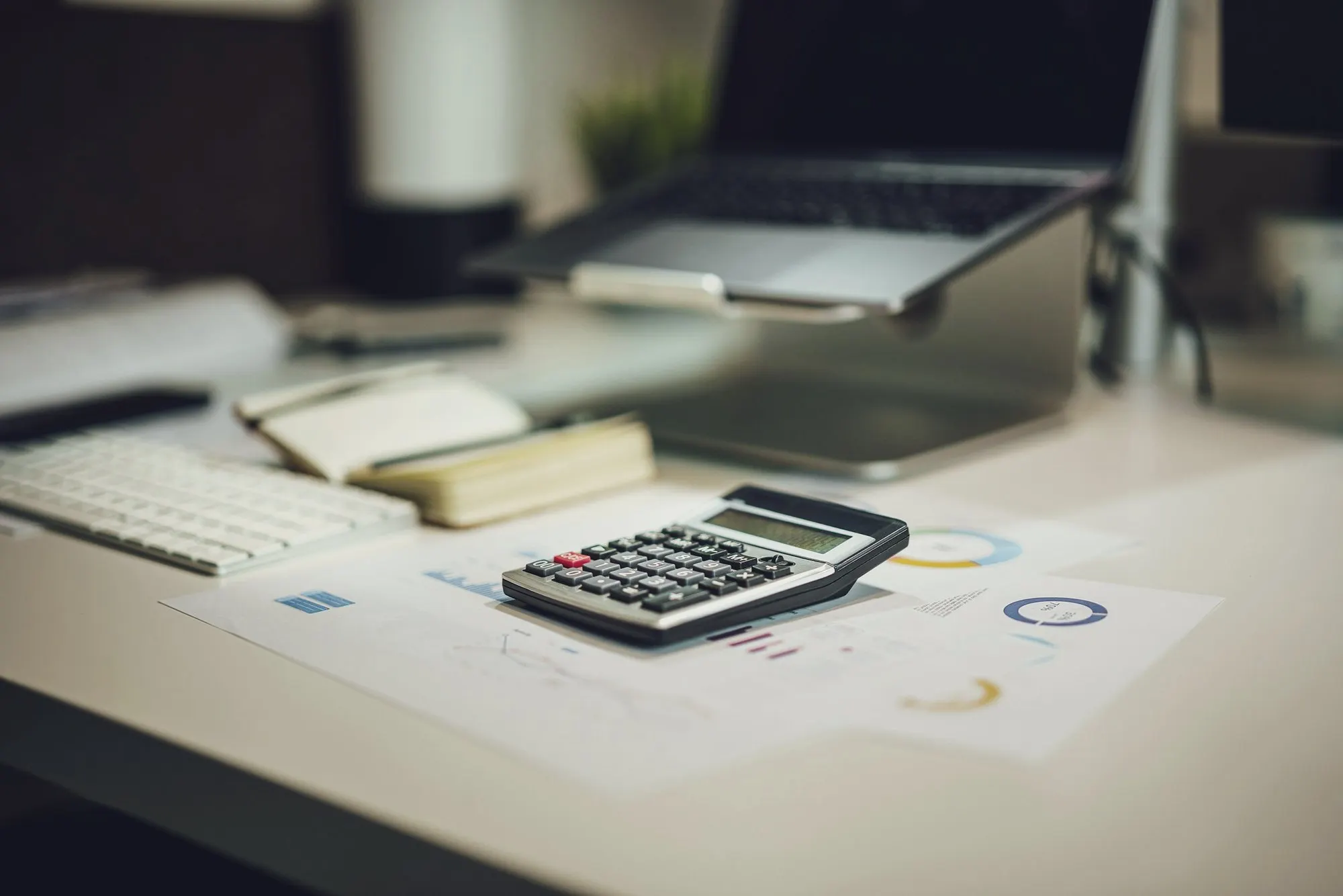 A desk with a laptop, a calculator, notes and printed charts for planning a business.