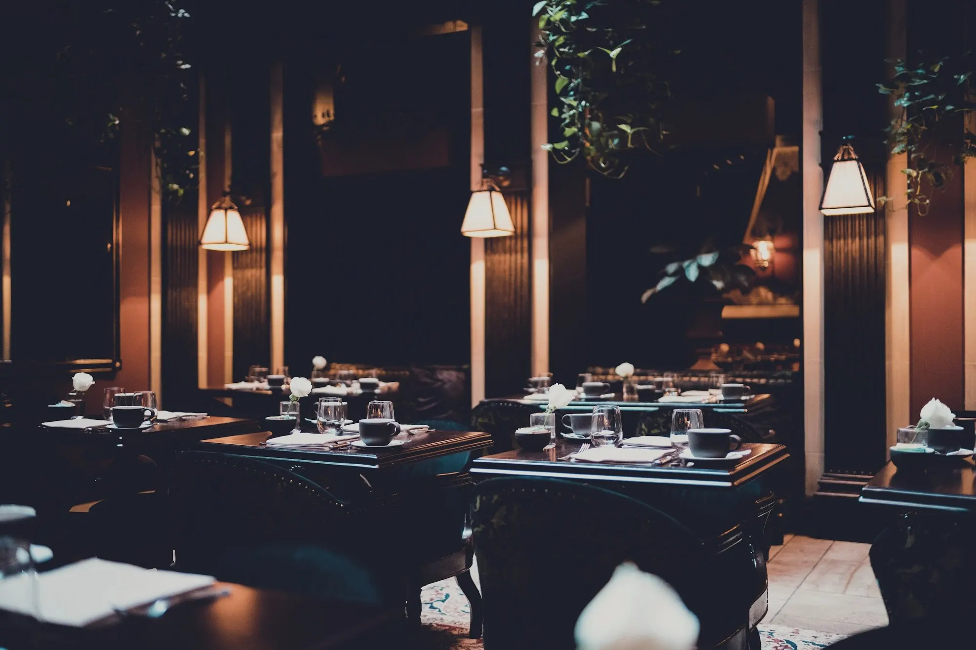 A dimly lit restaurant dining room with set tables and hanging pendant lamps.