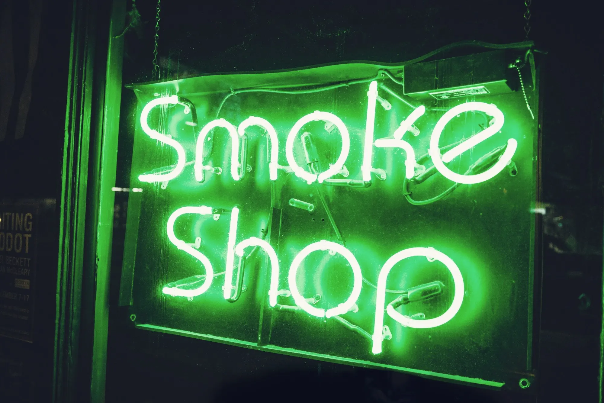 A glowing green neon smoke shop sign hanging in a dark window.