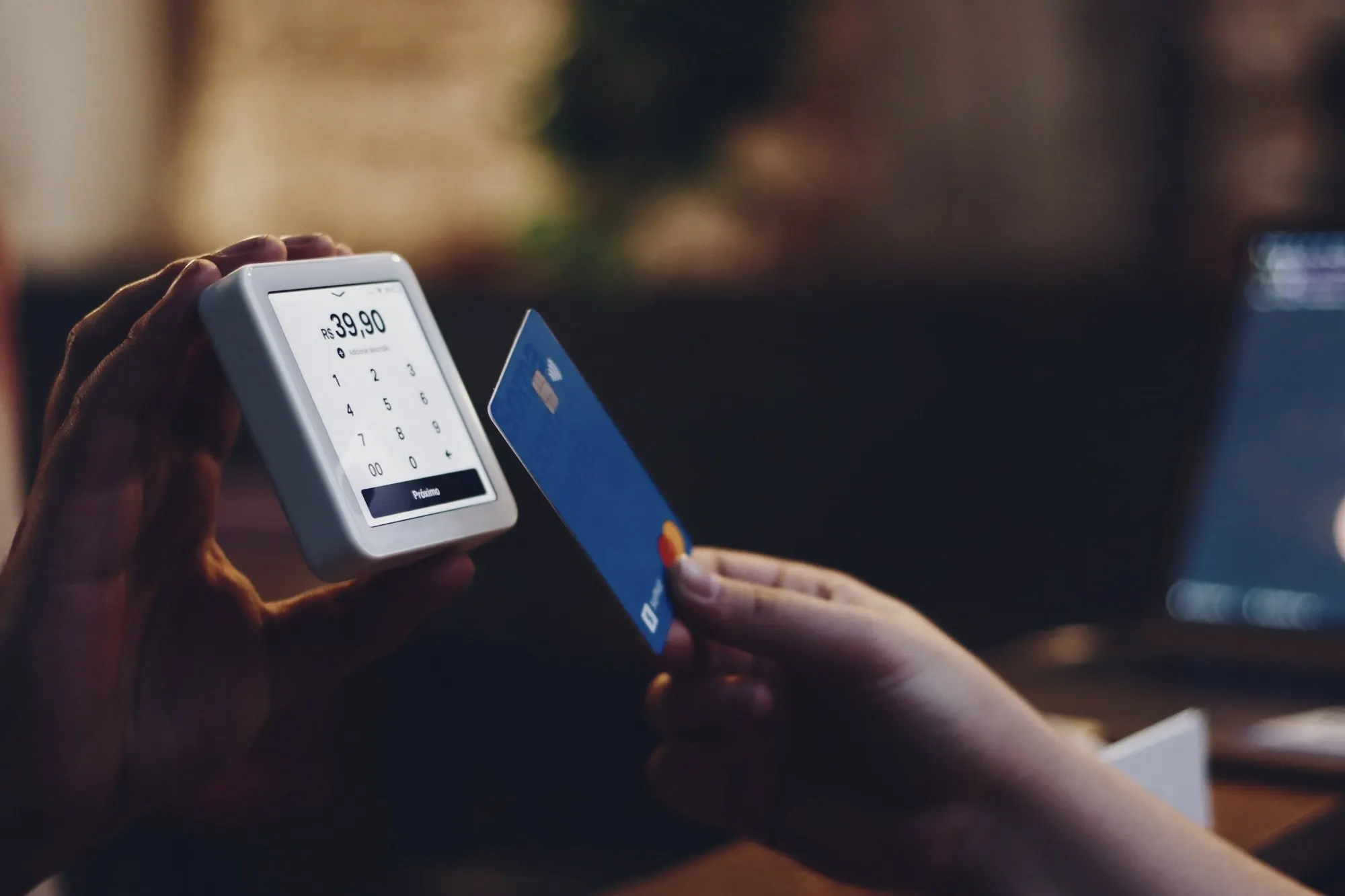 A hand holds a card beside a small handheld card terminal.