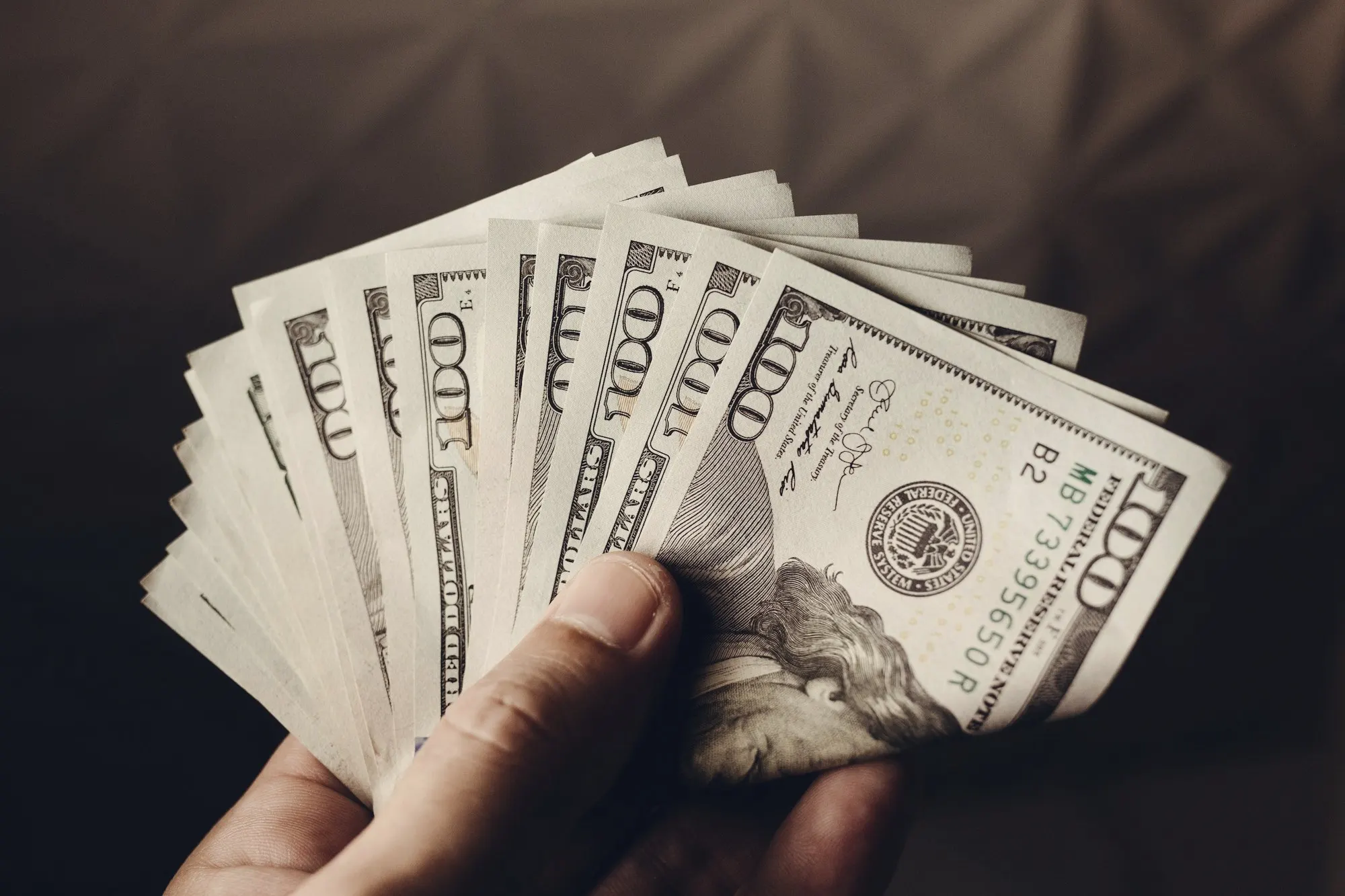 A hand fanning out a stack of hundred-dollar bills.