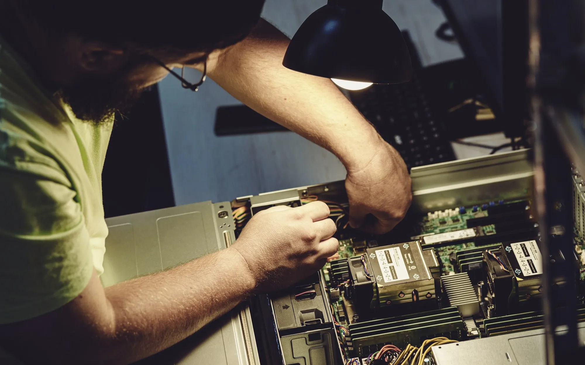 A technician working on the internal components of an open machine under a lamp.