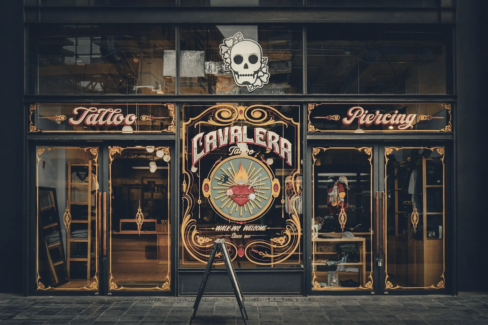 An ornate tattoo and piercing studio storefront with gold-trimmed display windows.