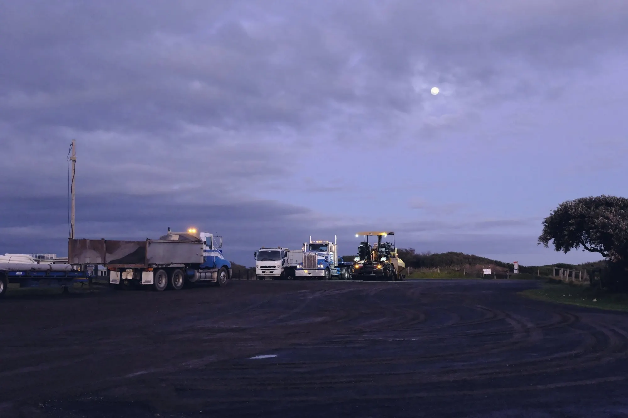Semi trucks parked at a truck stop under a purple dusk sky.